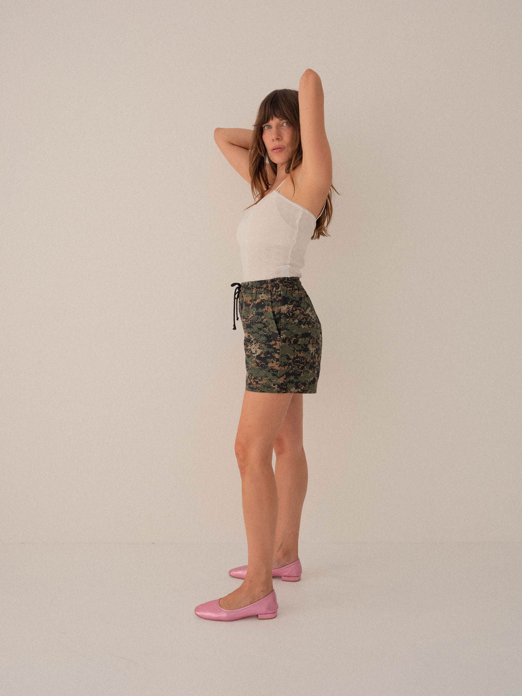 Woman wearing a white top and camouflage skirt on a plain background