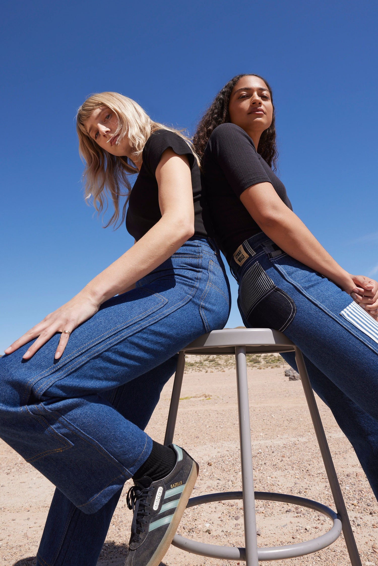 two friends sit on a stool outside wearing matching black t-shirts and classic indigo workwear jeans